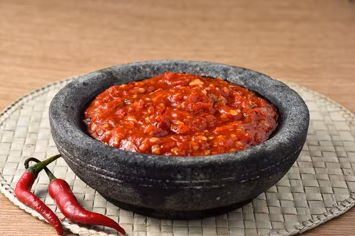 Spicy red salsa in a rustic stone bowl accompanied by fresh red chili peppers, featured in a Panamanian cooking class.