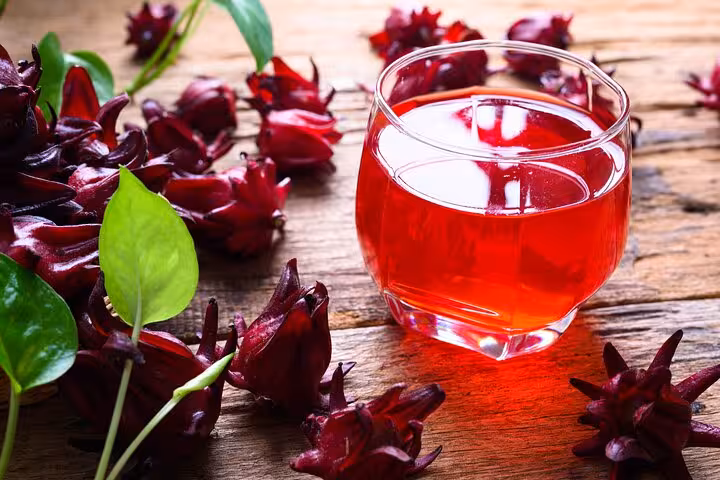 A vibrant glass of hibiscus drink surrounded by flowers, showcasing a refreshing recipe from the Panamanian class.