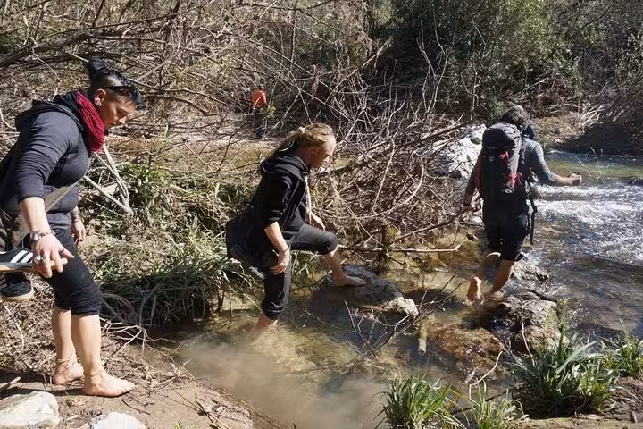 Adventurous hikers crossing a stream during a full-day tour of Pantalica, Sicily, surrounded by lush vegetation.