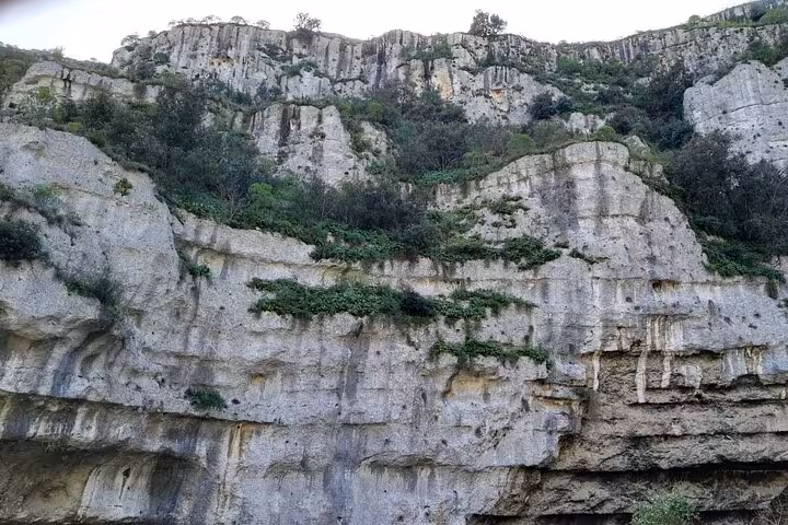 Majestic limestone cliffs rise above the lush greenery of Pantalica, showcasing Sicily's stunning natural beauty.