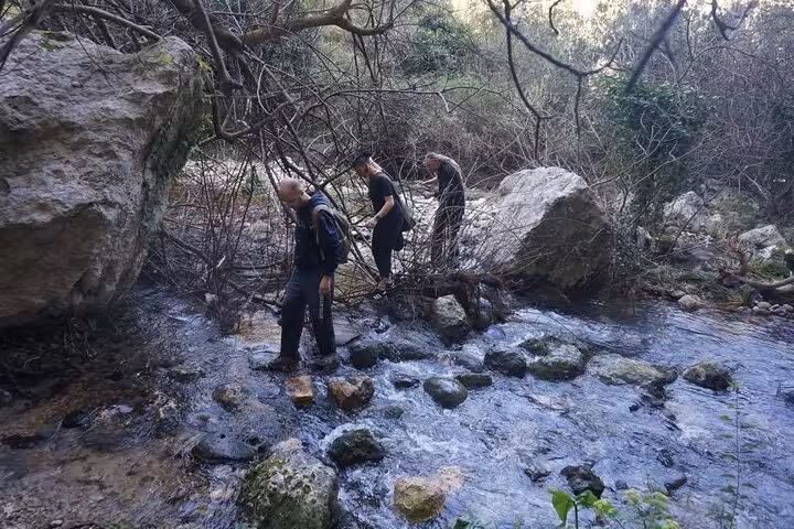 Adventurers crossing a rocky stream in Pantalica, experiencing the natural beauty of Sicily's renowned nature reserve.