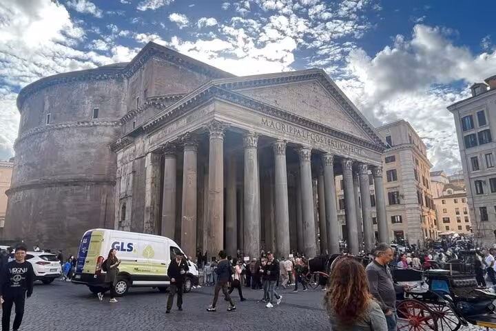 Side angle of the Pantheon with bustling tourists and a delivery van, highlighting its historic architecture.