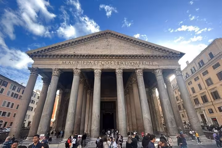Front view of the Pantheon in Rome with visitors, showcasing its grand columns under a clear blue sky.