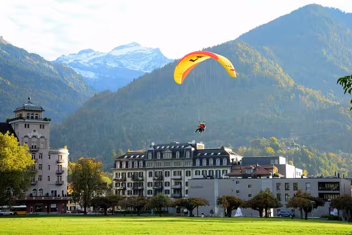 Paraglider soaring over picturesque Interlaken with majestic mountains in the background on the scenic Milan transfer.