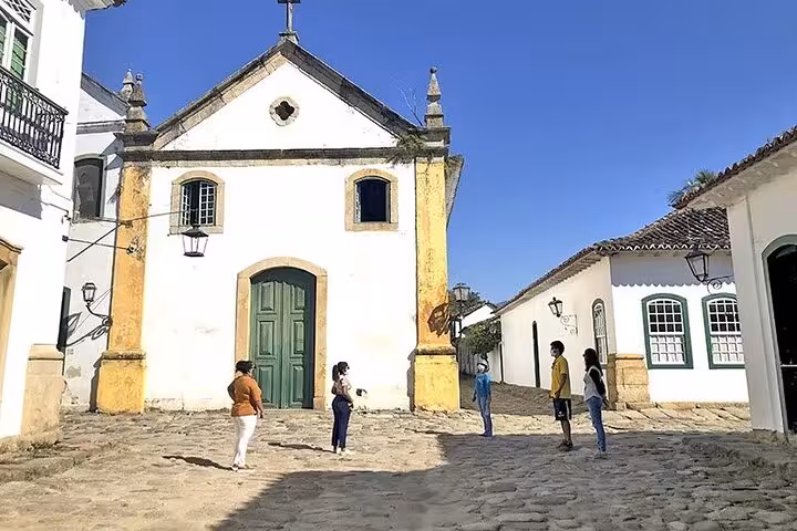 Tourists exploring the cobblestone streets and colonial church in Paraty's historic center on a sunny day.