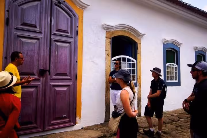 Tour guide explaining history to visitors outside a colorful colonial building in Paraty's historical center.