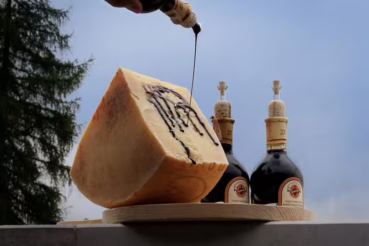 Aged Parmigiano-Reggiano cheese drizzled with balsamic vinegar, showcased with bottles on a wooden platter.