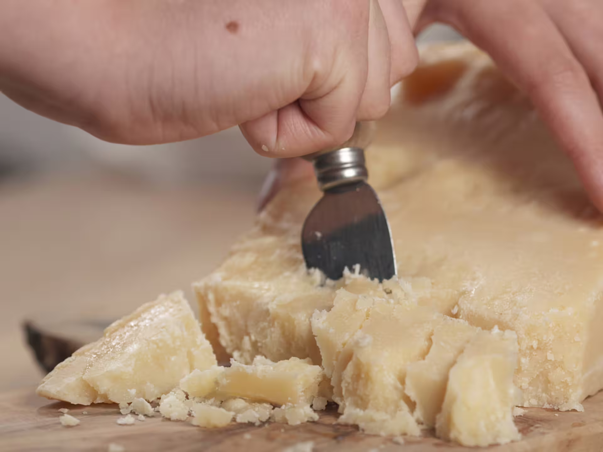 Close-up of hands cutting Parmigiano-Reggiano cheese, highlighting the rich texture and authentic flavor.