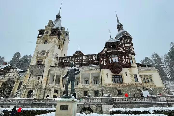 Peles Castle covered in snow with bronze statue in foreground, Sinaia Romania in winter