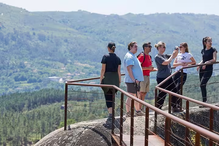 Group of tourists taking photos from a scenic viewpoint in Peneda-Gerês National Park, overlooking expansive forested hills.