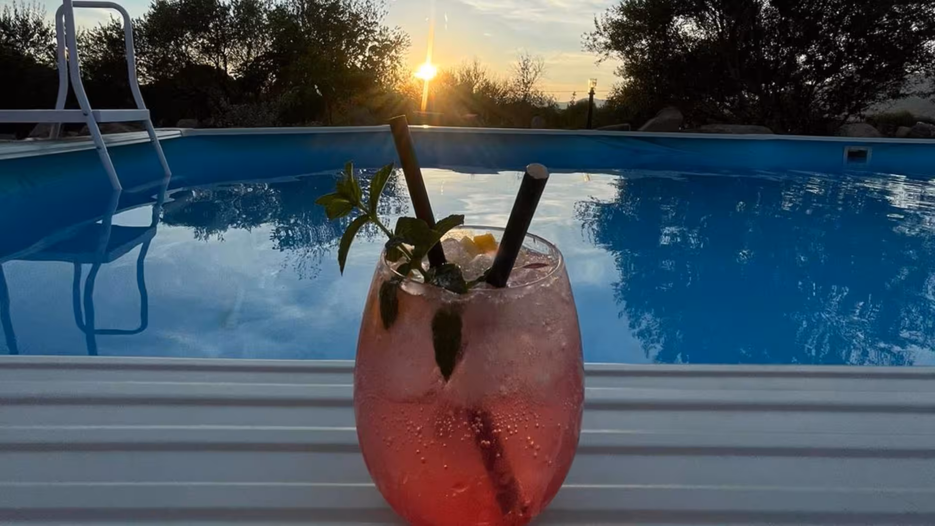 Refreshing cocktail by the pool at sunset during Perfugas glamping experience in nature, offering relaxation and tranquility.