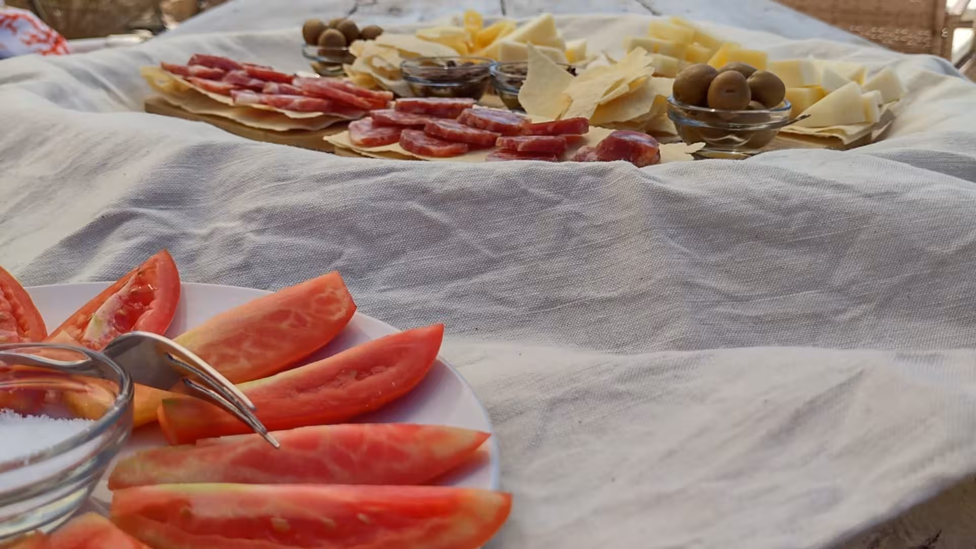 Gourmet charcuterie board with sliced tomatoes, cheeses, meats, and olives at Perfugas glamping experience.