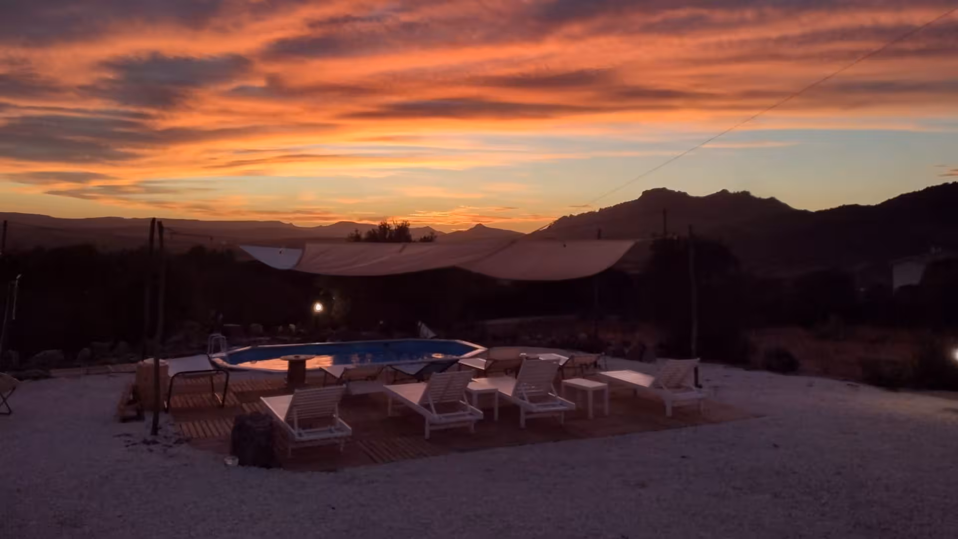 Stunning sunset view over a tranquil pool area at Perfugas glamping site, surrounded by serene nature landscapes.