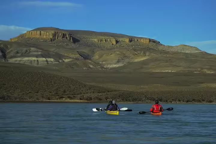 Kayakers paddle on La Leona River with stunning Patagonian mountains in the background, El Calafate adventure tour.