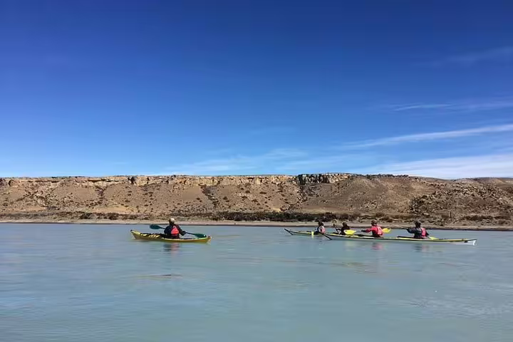 Kayakers paddle along the serene La Leona River with rugged cliffs under a clear blue sky in El Calafate.