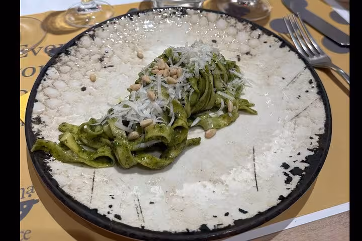 Plate of freshly prepared pesto pasta garnished with cheese and pine nuts from a cooking class in Florence.