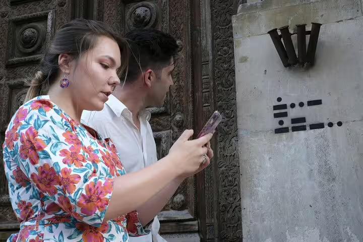 Two tourists using smartphone to scan mysterious morse code clues on historic stone wall during ghost walking tour