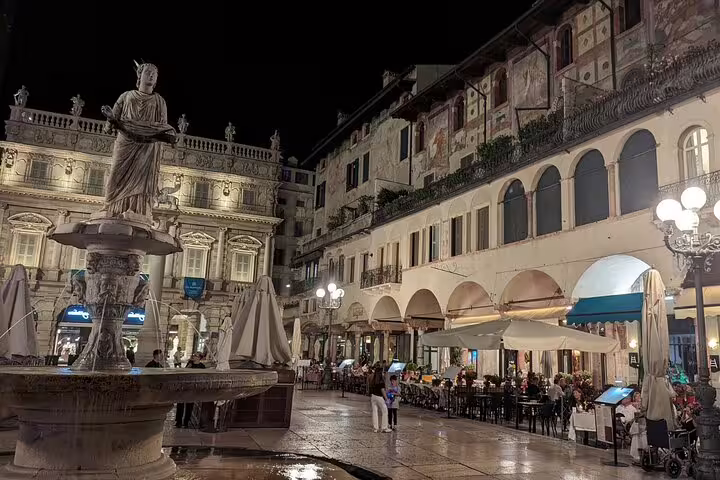 Piazza delle Erbe at night in Verona with fountain and cafes, featured stop on live guided walking tour
