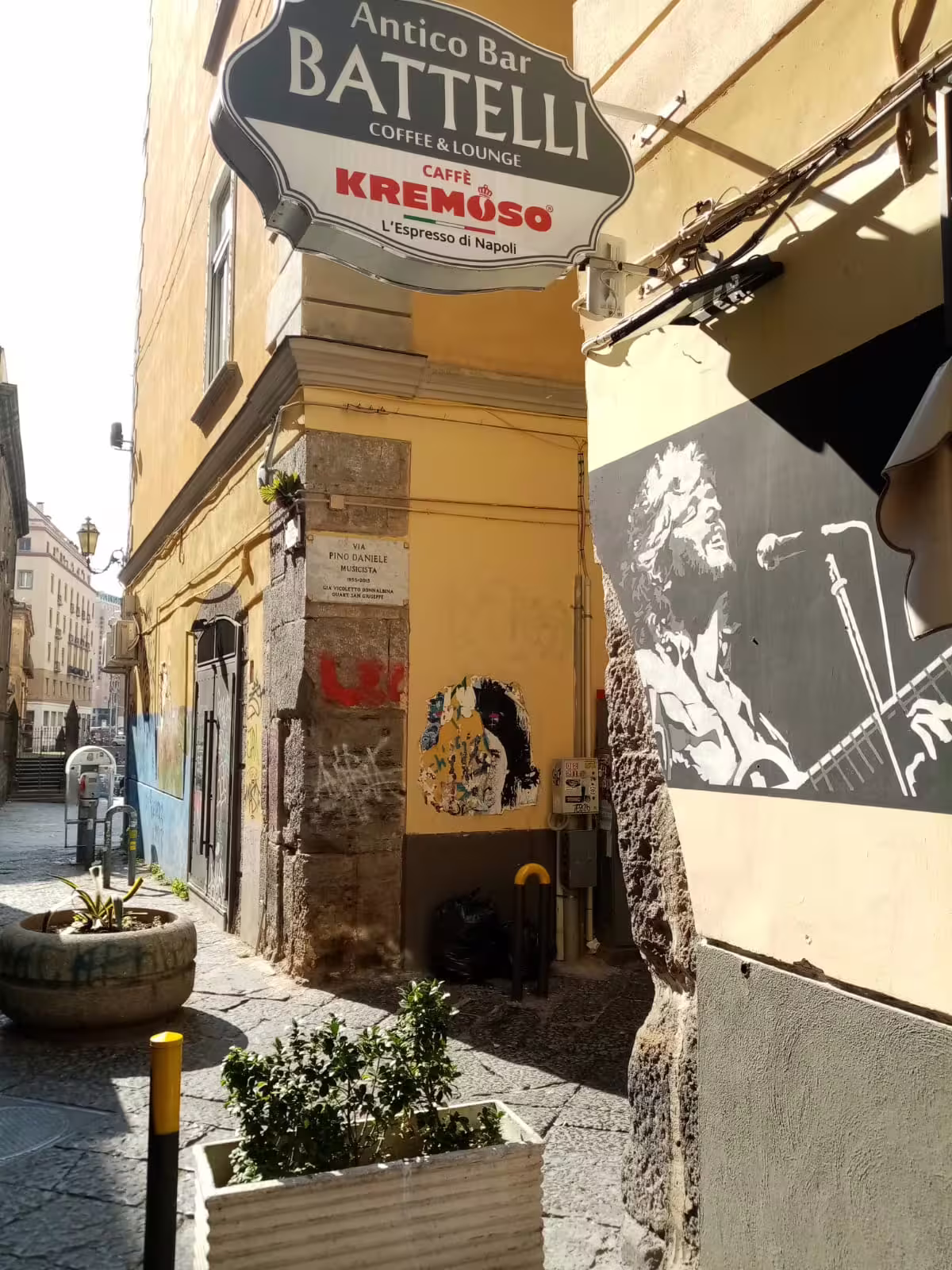 Narrow historic alley in Naples with Pino Daniele mural and Antico Bar Battelli sign on guided music walking tour