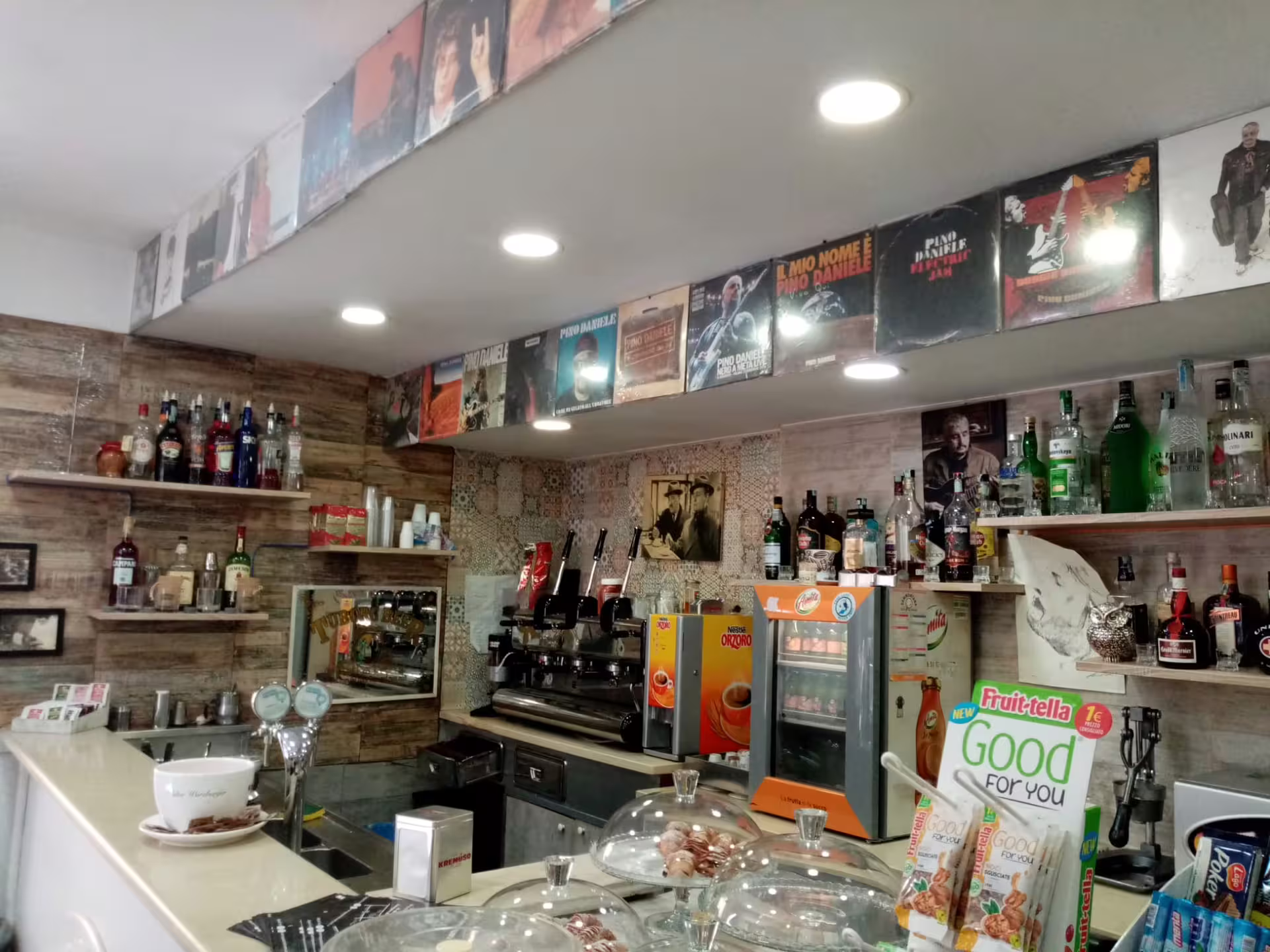 Vintage Neapolitan bar lined with Pino Daniele album covers, espresso machines and liqueurs on music history walking tour