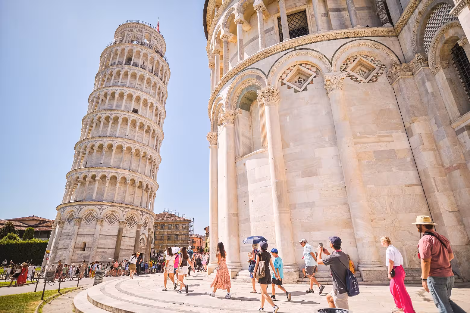 Tourists exploring Piazza dei Miracoli with the Leaning Tower of Pisa on a sunny day during a Florence day trip.