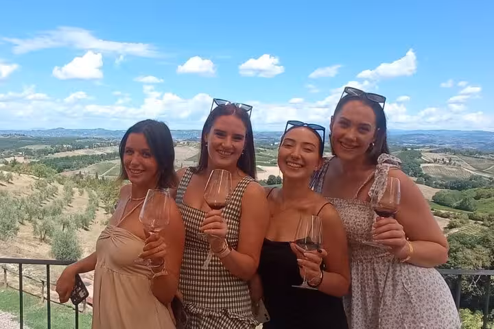 Four women enjoying a wine tasting with scenic Tuscany vineyards in the background, part of a Pisa Vinci tour.