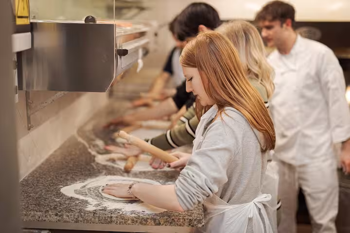 Participants rolling dough in a lively pizza cooking class near Piazza Navona, Rome.