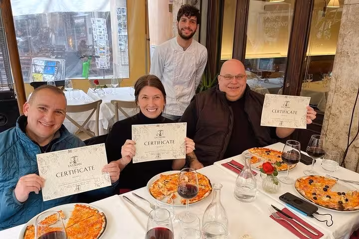 Participants proudly display certificates after completing a pizza cooking class in Rome near Piazza Navona, enjoying their creations.