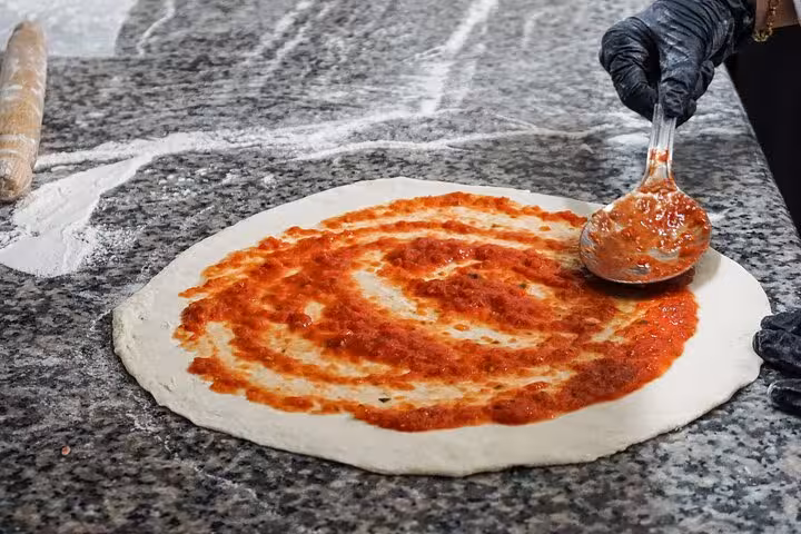 Pizza dough topped with rich tomato sauce being prepared in a Rome cooking class.