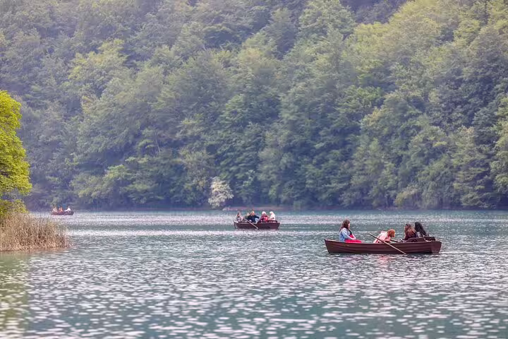 Visitors boating on calm lake at Plitvice Lakes National Park, Croatia, with lush forest backdrop, entry ticket