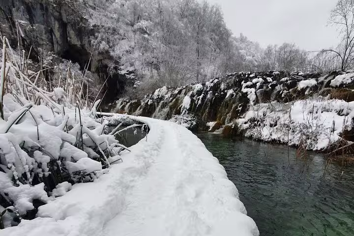 Snow-covered path beside turquoise water and cascades at Plitvice Lakes, Croatia, tour with train and boat ride