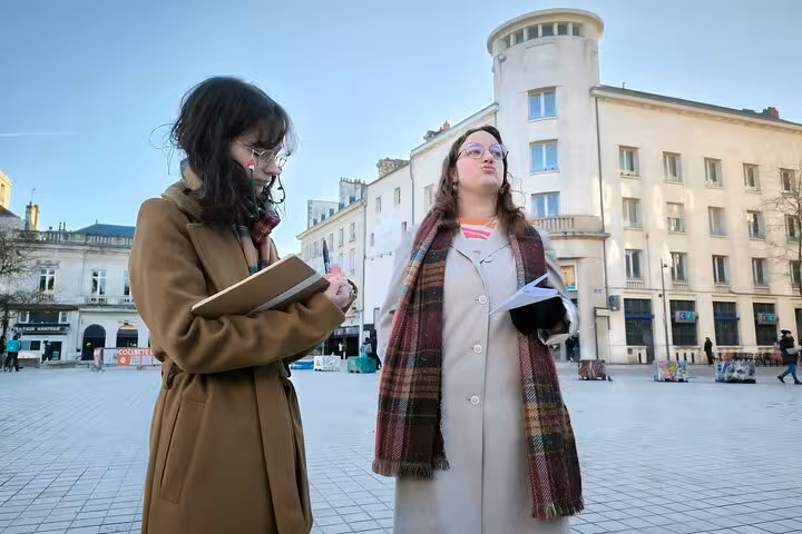 Two women discuss heritage sites on a sunny day in Poitiers' bustling city square during a guided walking tour.