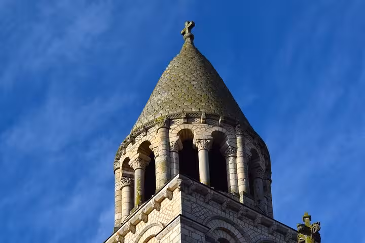 Close-up of a historic stone tower with a conical roof in Poitiers, showcasing medieval architecture under a blue sky.