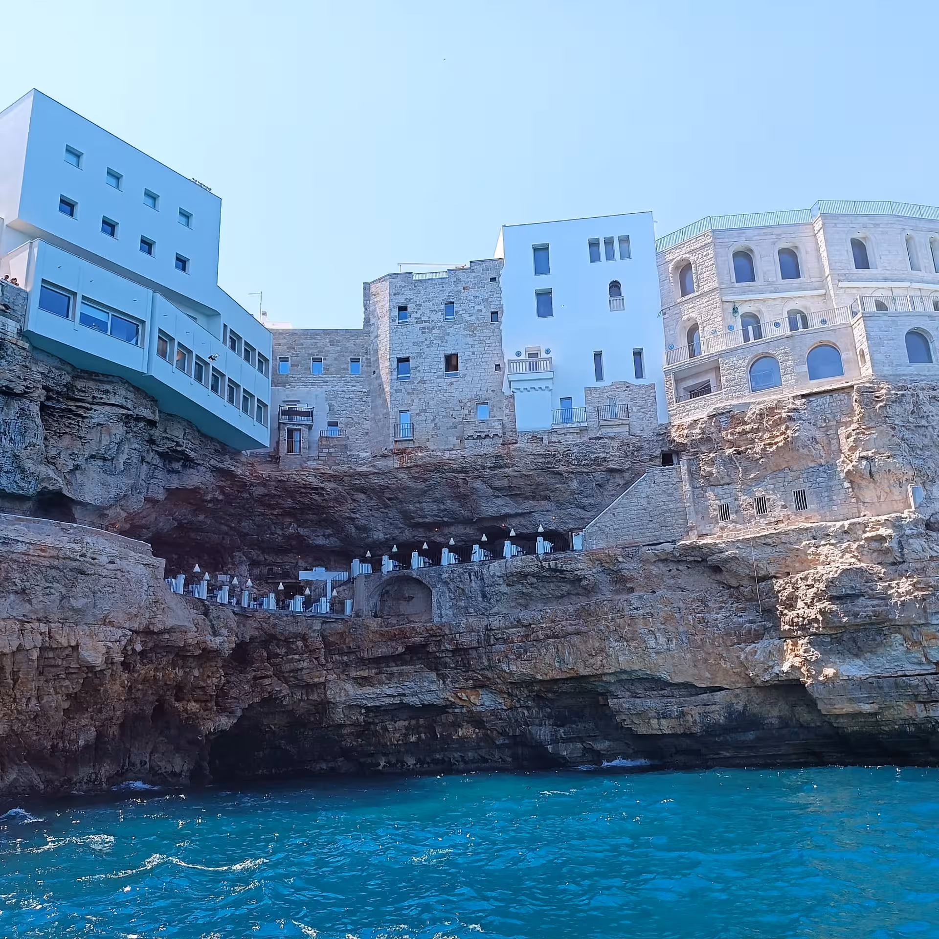 Scenic view of Polignano a Mare's iconic cliffside buildings above sea caves during a boat tour.