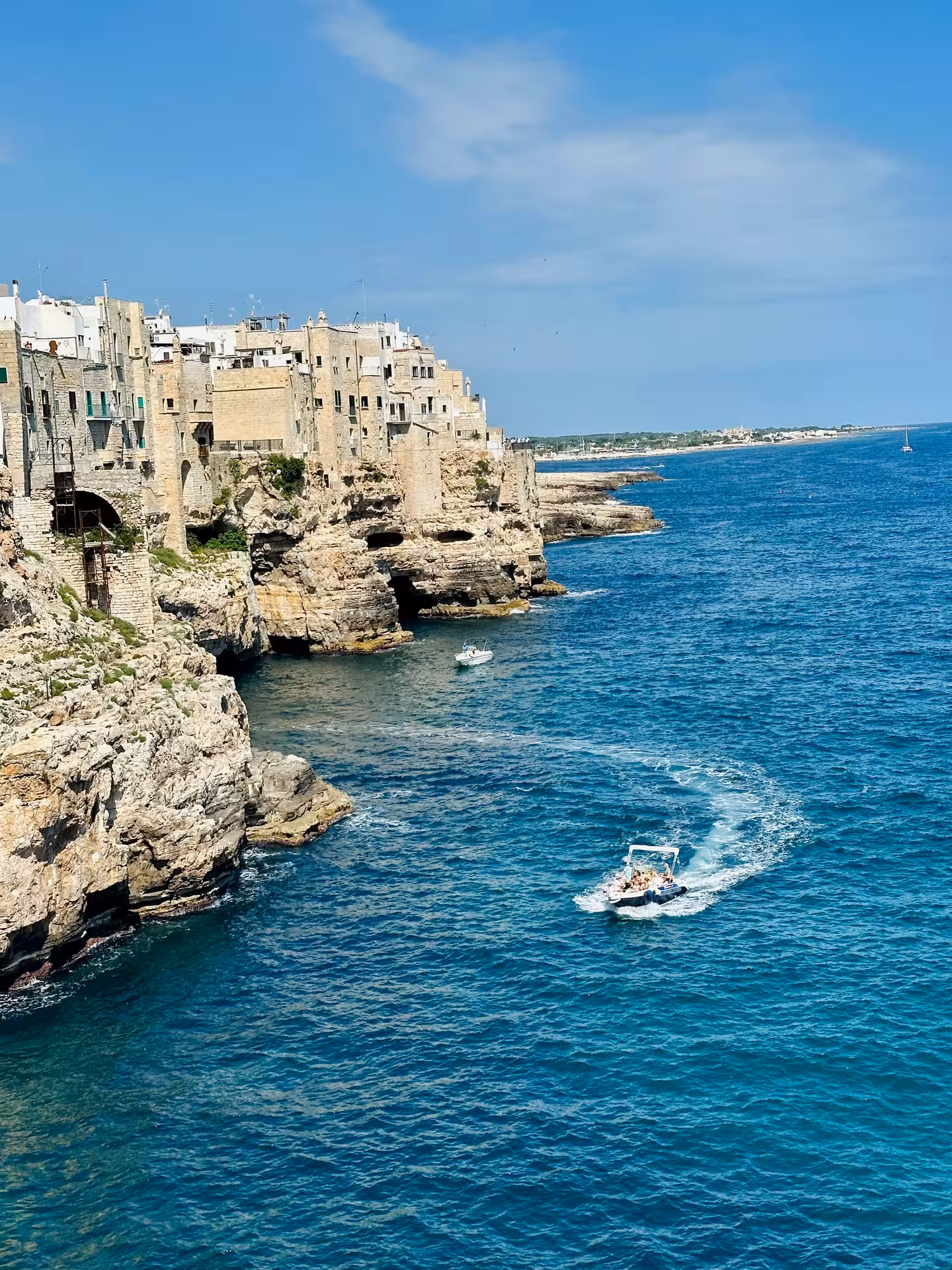 Boat navigating turquoise waters near rocky cliffs in Polignano a Mare, showcasing picturesque coastal architecture.