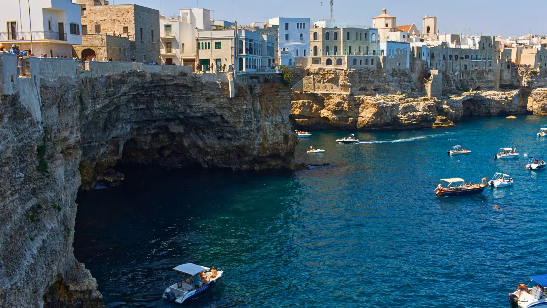 Numerous boats exploring sea caves beneath historic cliffside buildings in Polignano a Mare, perfect for a scenic tour.