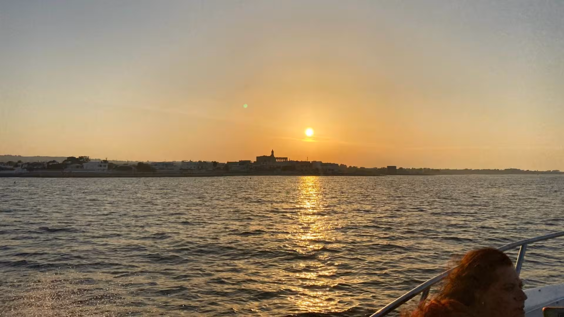 Sunset view from a boat tour in Polignano a Mare with sparkling water and distant coastline.
