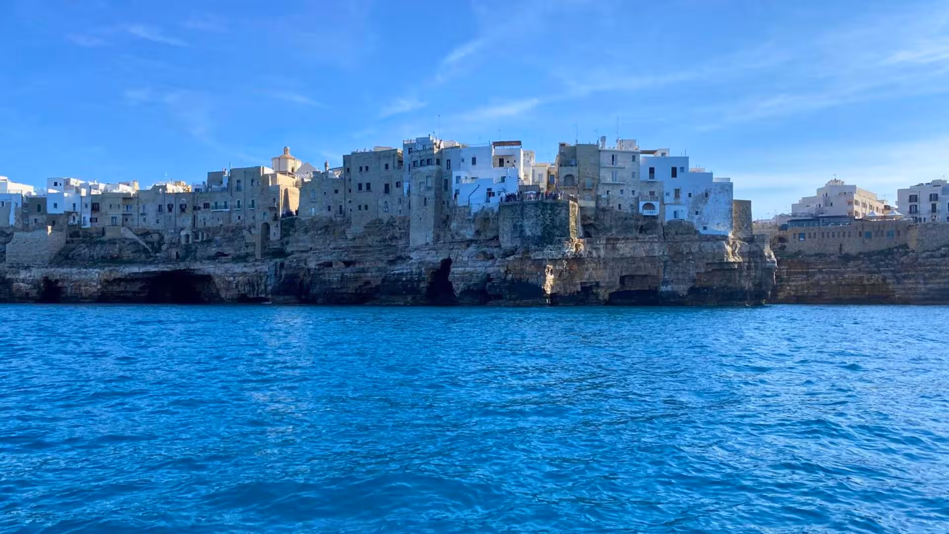View of Polignano a Mare's cliffside historic town from a boat on the clear blue Adriatic Sea.