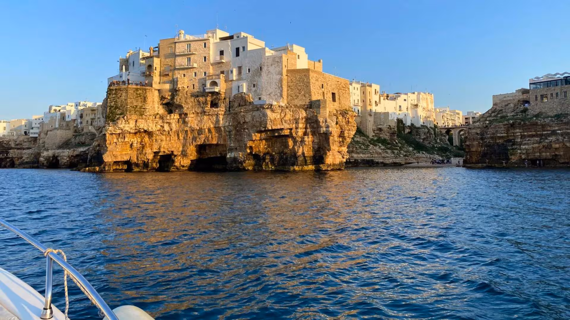 Golden sunset illuminating Polignano a Mare's historic cliffs and caves seen from a boat tour.