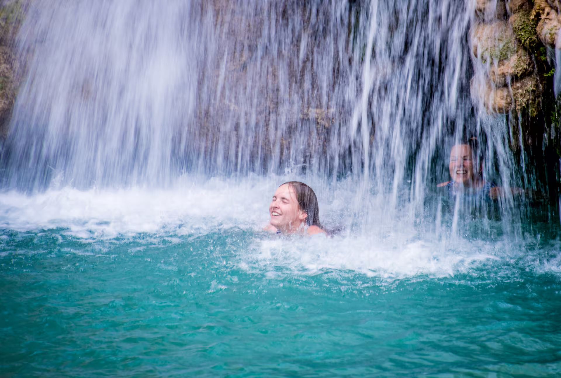 Swimmers enjoying the cool turquoise pool beneath Polylimnio Waterfalls on a guided hike in Messinia, Greece