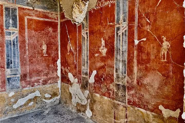 Vibrant frescoes adorn the ancient walls of a room in Pompeii, showcasing classical art on a guided tour from Positano.