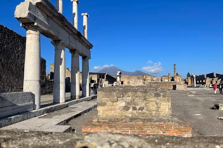 Ruins of ancient columns and architecture in Pompeii with Mount Vesuvius in the background, featured on the guided tour.