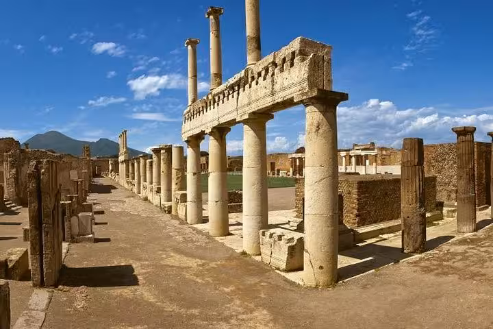 Ancient ruins of Pompeii with towering columns under a clear blue sky, highlighting historical exploration on the tour.