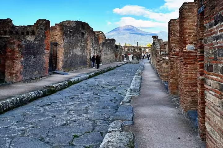 Cobblestone street in Pompeii with Mount Vesuvius looming in the background, showcasing ancient Roman architecture.