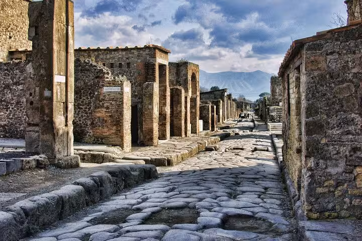 Scenic view of ancient Pompeii's cobblestone street with towering ruins, ideal for a Vesuvius and Amalfi experience.