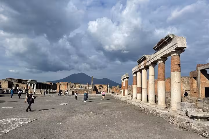 Tourists explore the ancient ruins of Pompeii with Mount Vesuvius in the background on a skip-the-line guided tour.