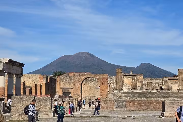 Tourists explore Pompeii ruins with Mount Vesuvius in the background on a guided tour from Sorrento including lunch.