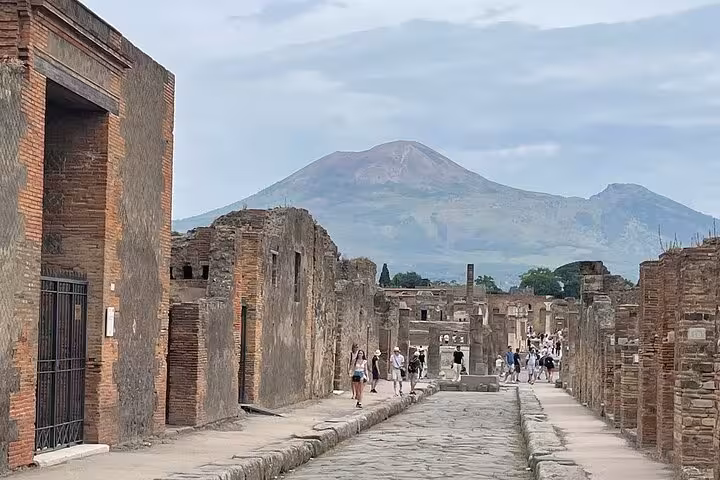 Historic Pompeii street with Mount Vesuvius looming, part of a guided tour from Sorrento featuring lunch.