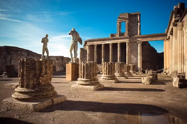 Ancient ruins of Pompeii with statues and pillars under a clear blue sky on the Amalfi Coast tour.