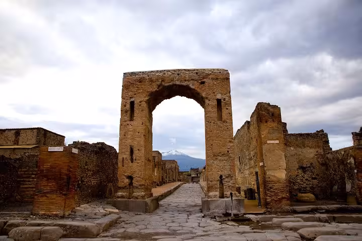 Discover the historic archway and cobblestone streets of Pompeii with stunning Mount Vesuvius in the background.